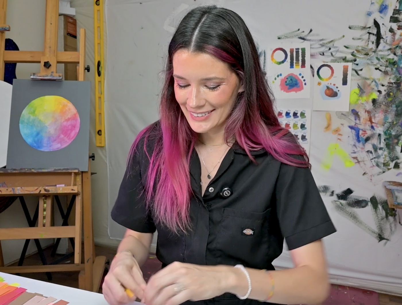 Sari Shryack smiling next to a hand-painted color wheel, with color theory reference sheets in the background